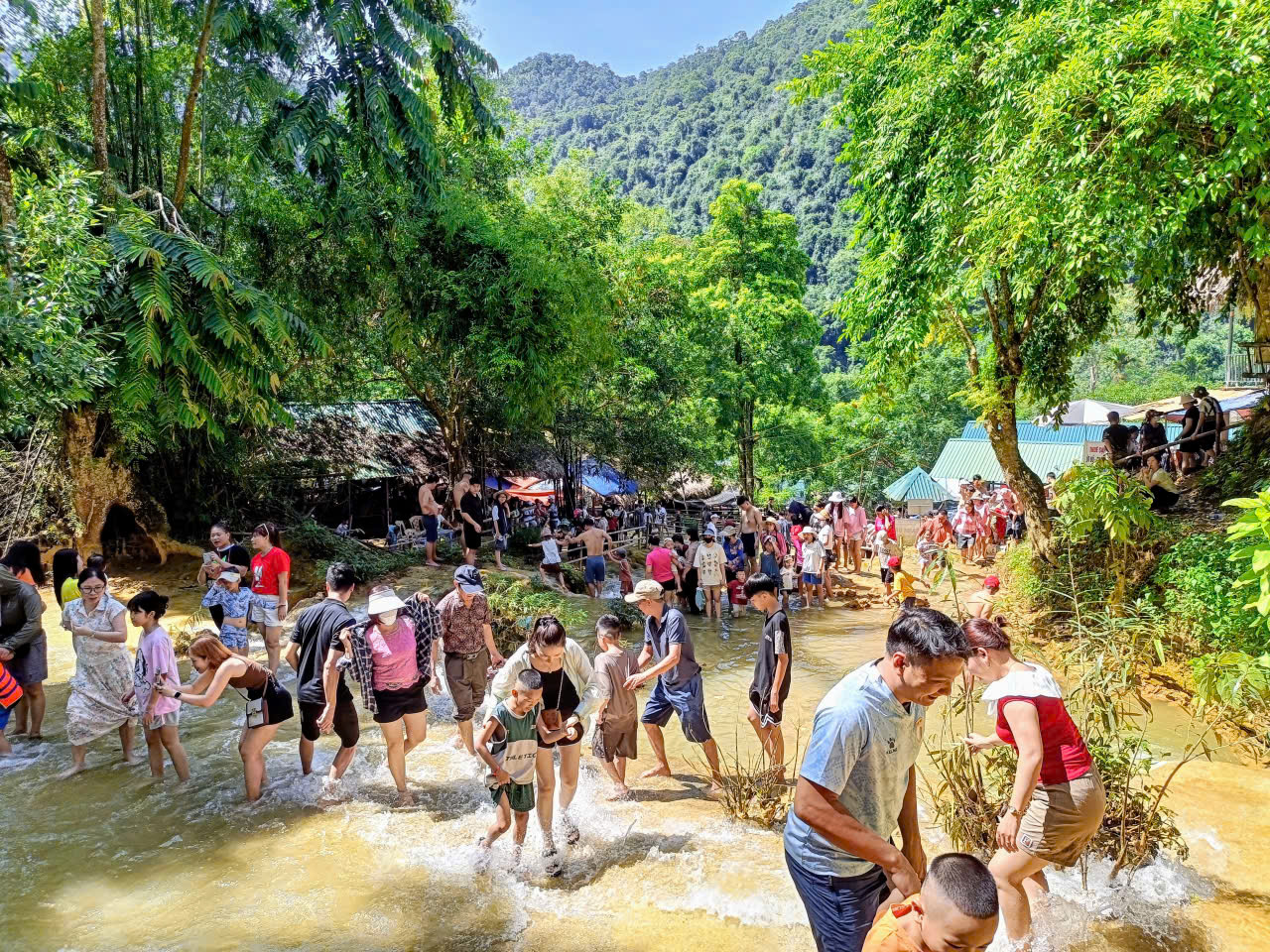 Du khách các độ tuổi hào hứng lội suối, khám phá bản làng dưới chân thác.